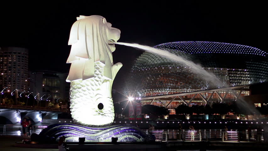 SINGAPORE - NOVEMBER 19: Merlion sculpture and one of the Esplanade twin domes at night on November 19, 2009 in Singapore. Some visitors to the viewing platform at Marina Bay walk in the background.