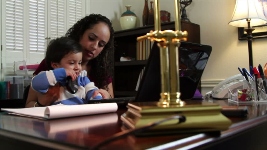 A pretty Hispanic mom in her home office with her little son sitting in her lap.