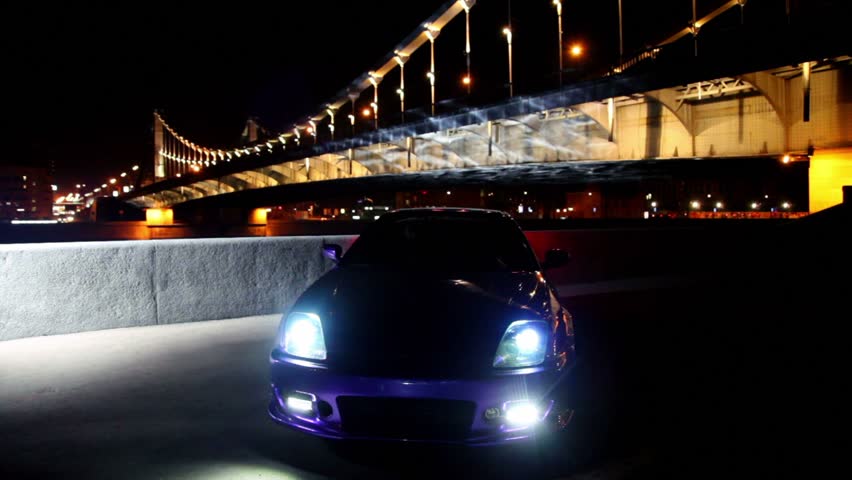 Car stand with parking lights blinks at background of bridge at night and then moves little forward