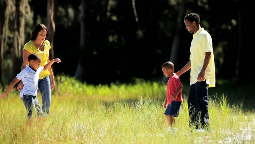 Happy young ethnic family having fun kicking a football together in the park