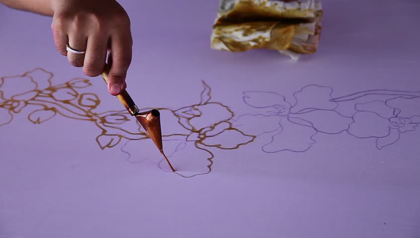 An artist carefully draw the flower motif on traditional batik fabric with melted wax