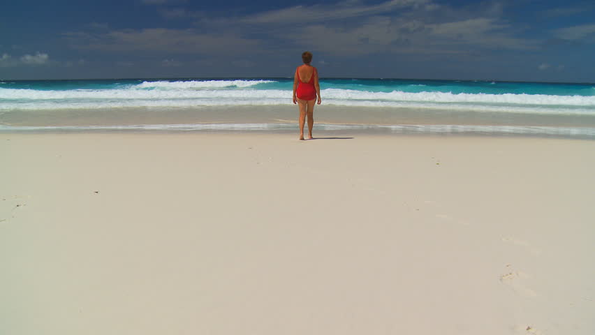 elderly woman in swimsuit walking alone on the beach to the sea