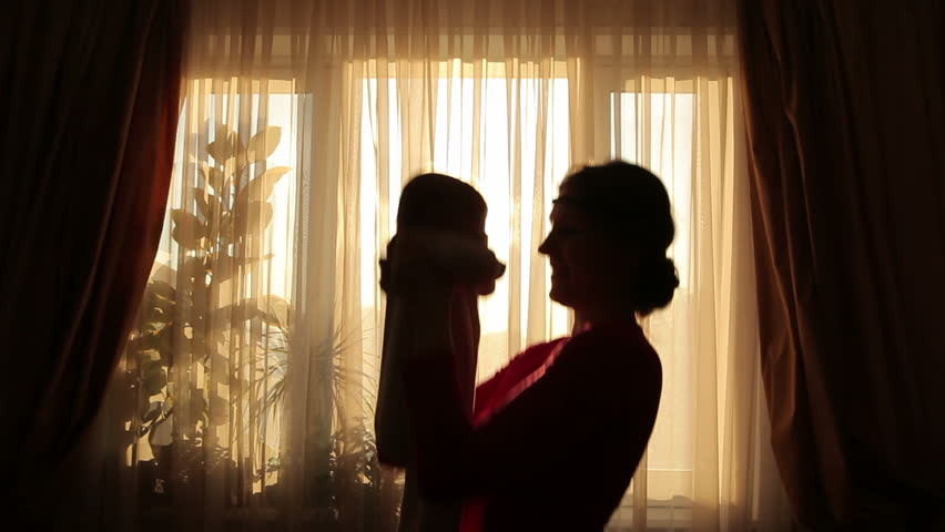 Mother plays with baby before window in silhouette