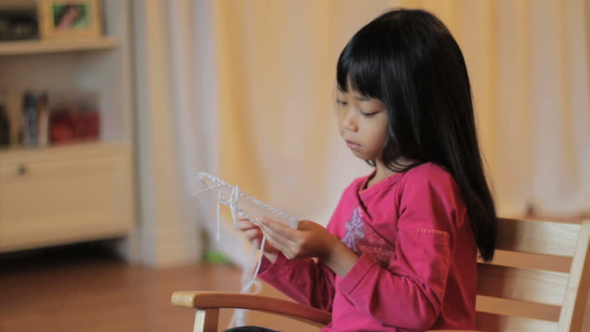A cute little 5 year old Asian girl enjoys doing some stitching in her rocking chair.