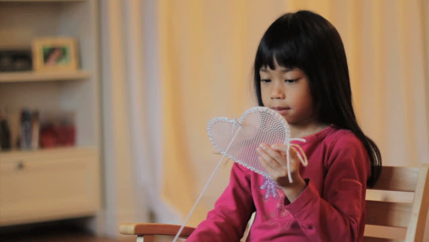 A cute little 5 year old Asian girl creates a beautiful heart shaped gift out of stitching just in time for Valentine's Day.