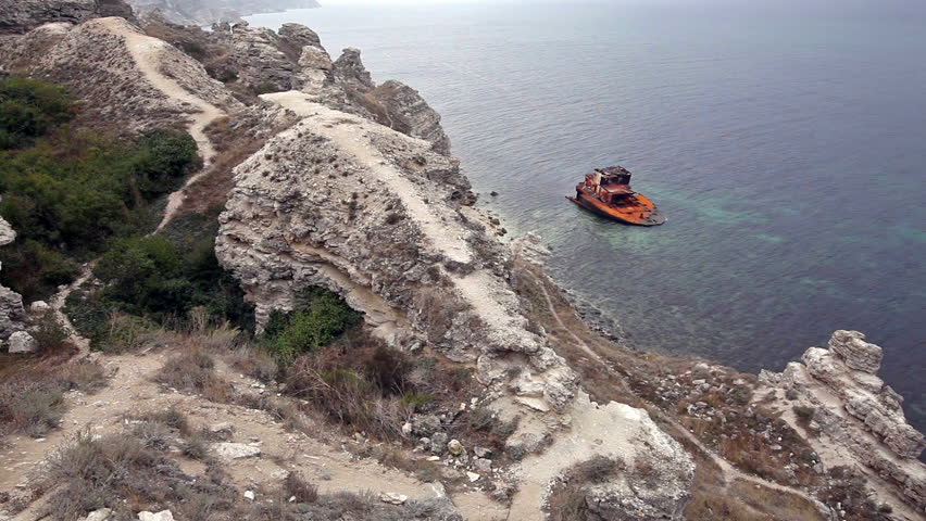 Rock with a foot footpath and the sea with the broken rusty ship