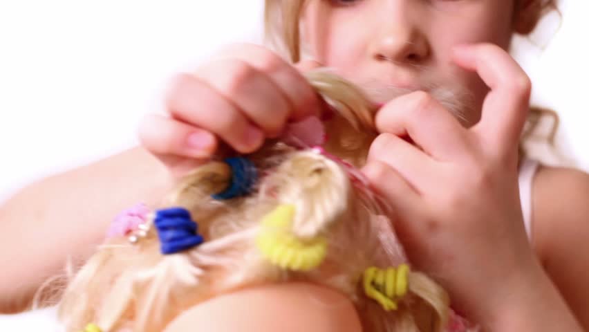 Little girl use elastic band to braid dolls hair, closeup view