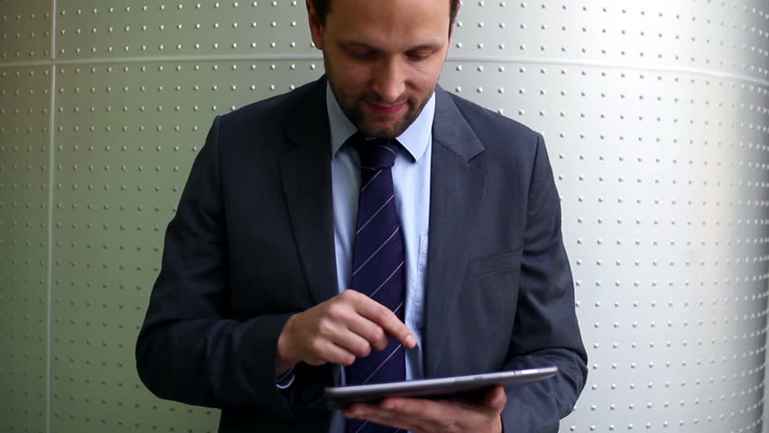 Young happy businessman with tablet computer by the wall