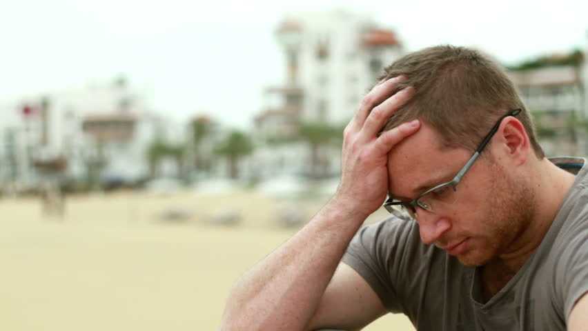 Sad pensive man sitting by the beach, outdoors