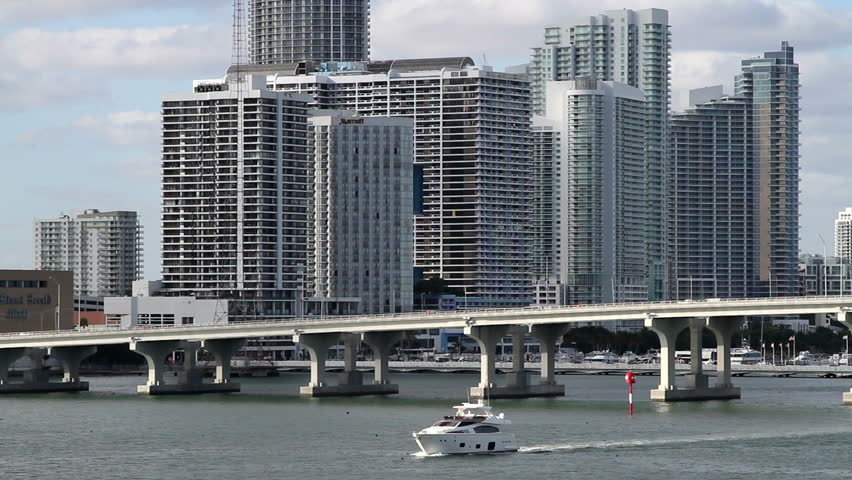Cityscape, Miami skyline with bridge, from over the water angle. A boat enters the scene, under the bridge