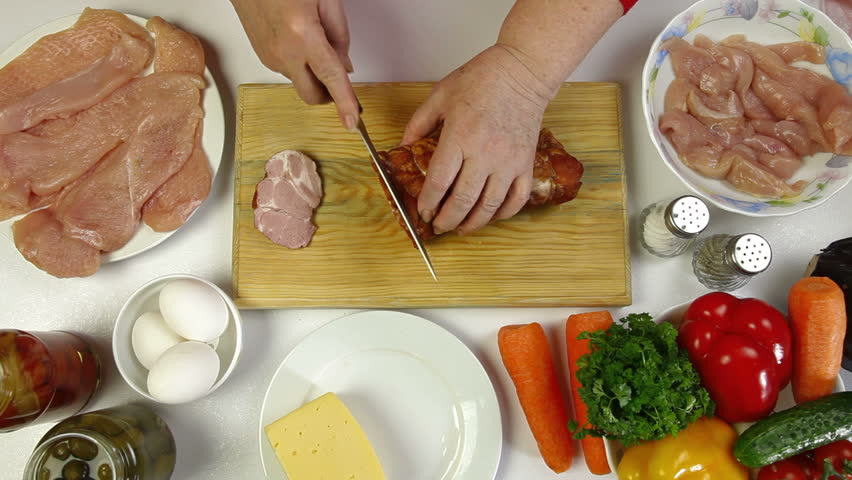 Women's hands slicing pork bacon, an ingredient for cooking chicken roll. Top view