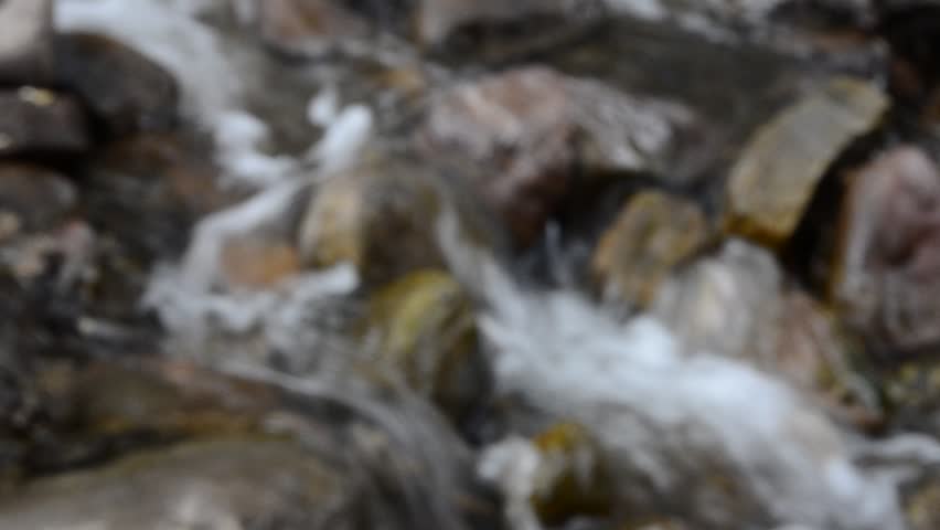 Mountain stream or creek flowing past mossy rocks - rack focus