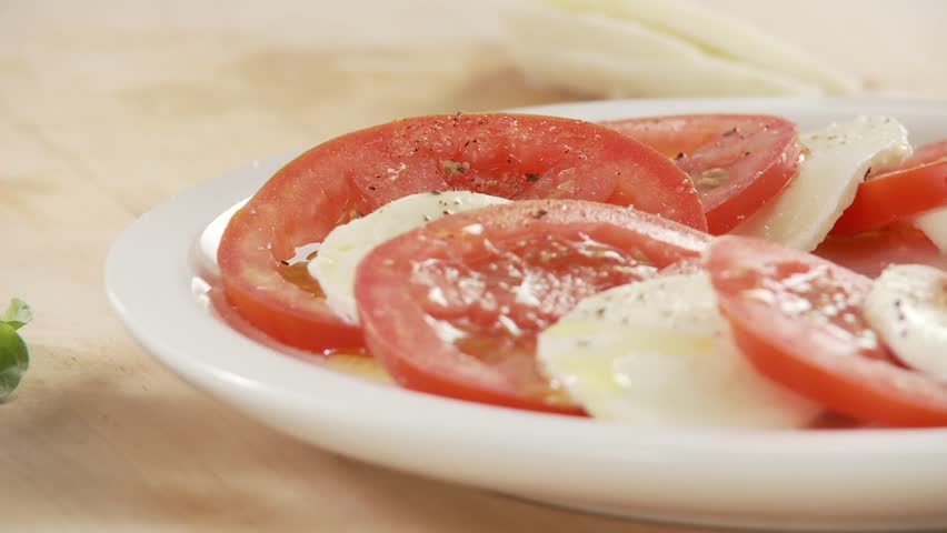 Tomato and mozzarella slices being drizzled with olive oil