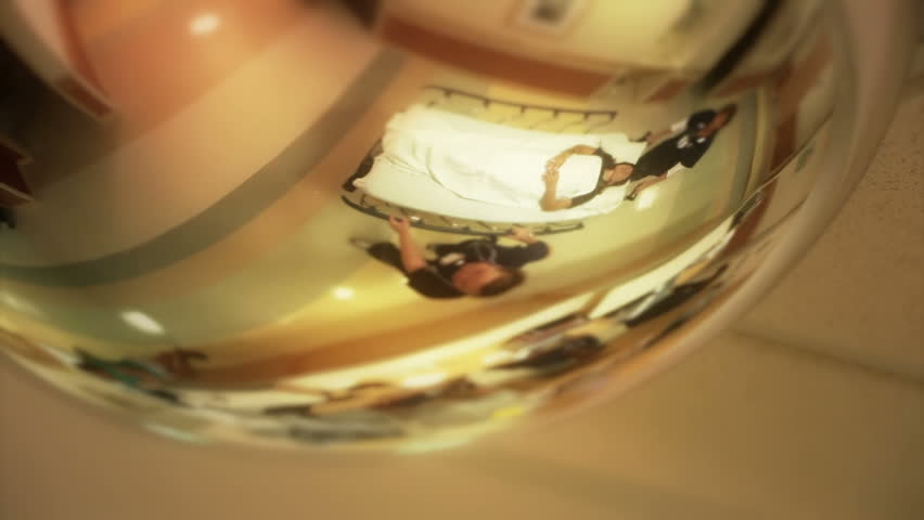 A patient gets wheeled down a hospital hallway.  As seen from the ceiling mirror.