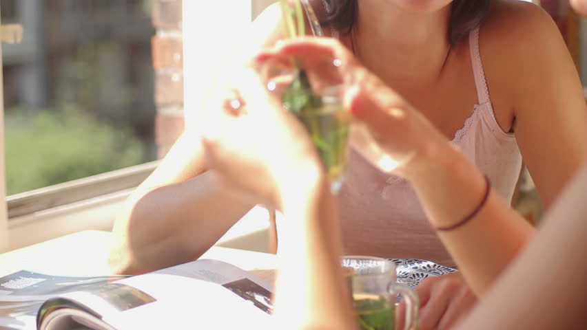 Female friends sitting at table eating cake drinking tea and laughing