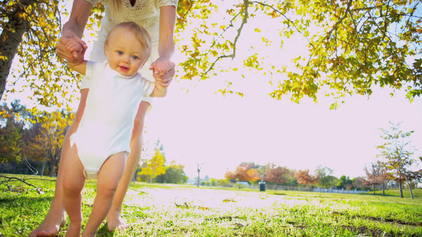 Young blonde mother holding her young child as he practices his first steps