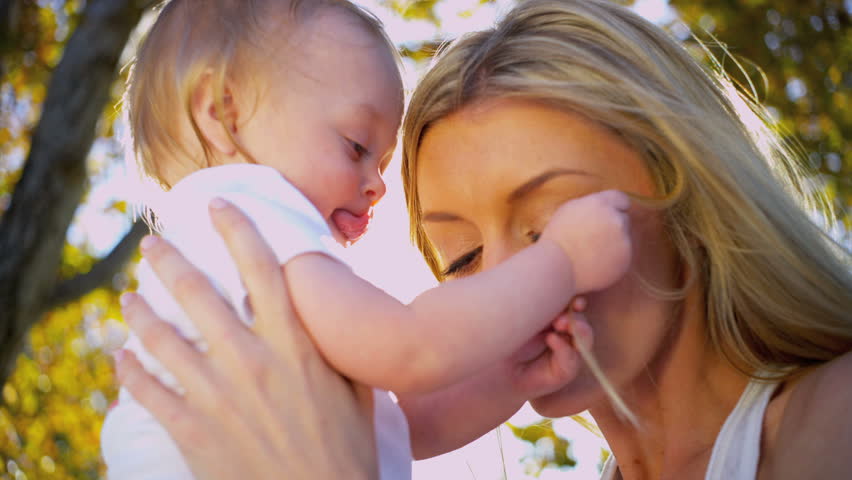 Young Caucasian mother outdoors holding her baby while he plays with her hair