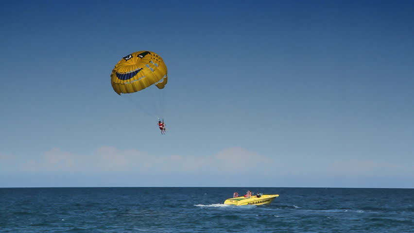 Person flying on a parachute is pulled on a rope by a boat.