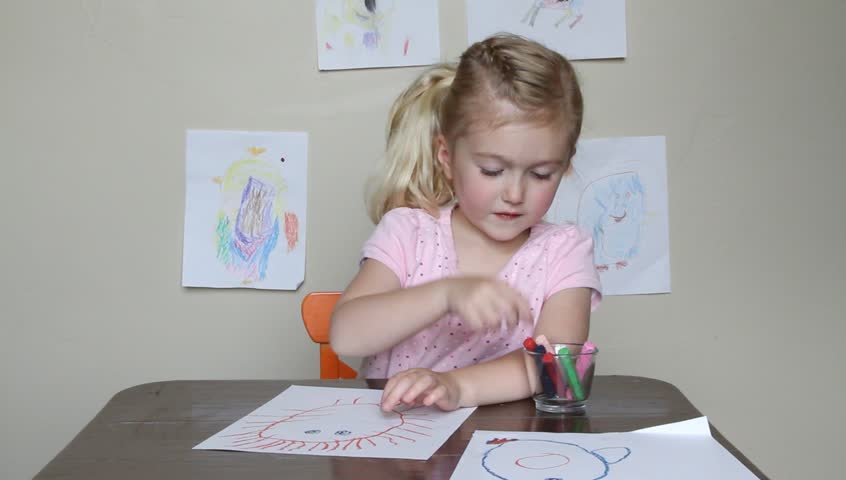 Young child drawing with crayons while sitting at desk