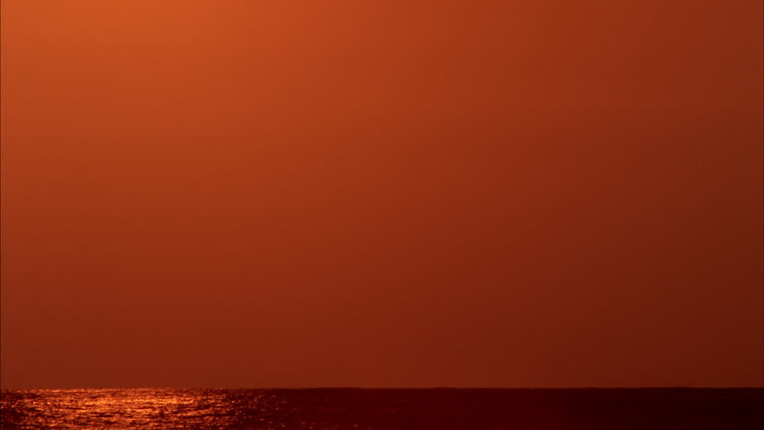 Sunset over Black Ocean Time-lapse - The sun slowly sets over the water as it pierces through smog and black sky.