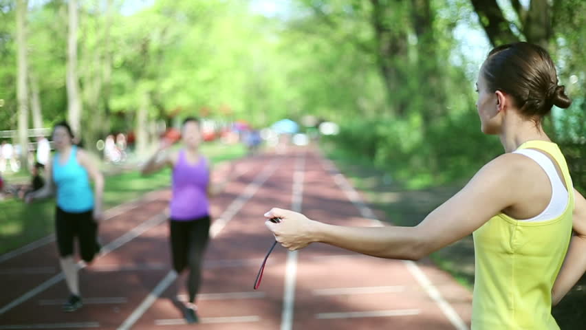 Women running on the track, trainer checking their time, slow motion
