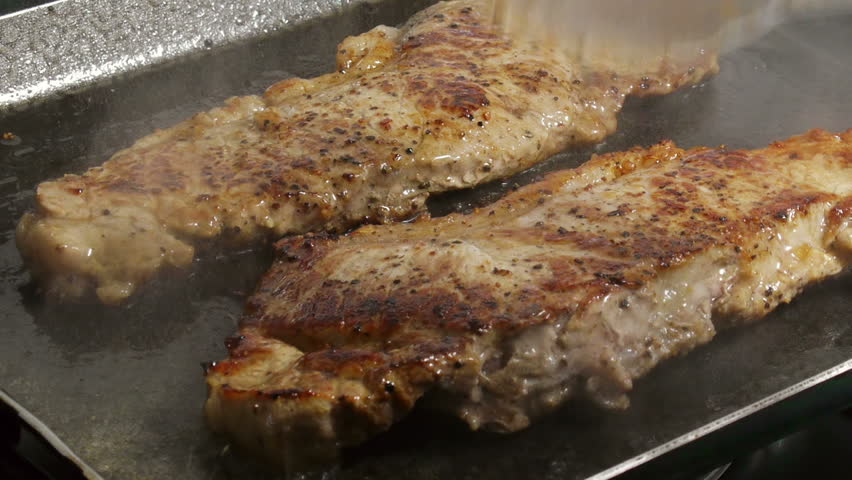 Cooking Steaks (HD). New York cut steaks being cooked and flipped on frying surface. Ambient audio included in the sequence.  