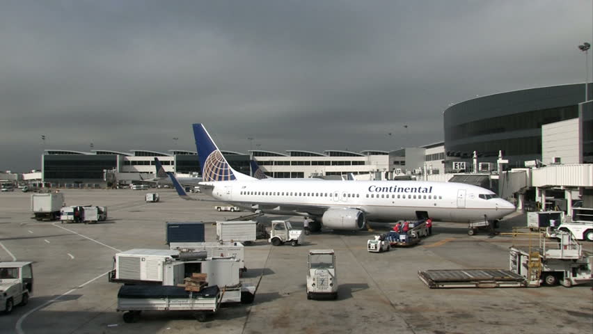 busy airport ramp with Continental aircraft having baggage unloaded. Building, ramp and utility vehicles and trucks driving around parked airplane. Houston International Airport.