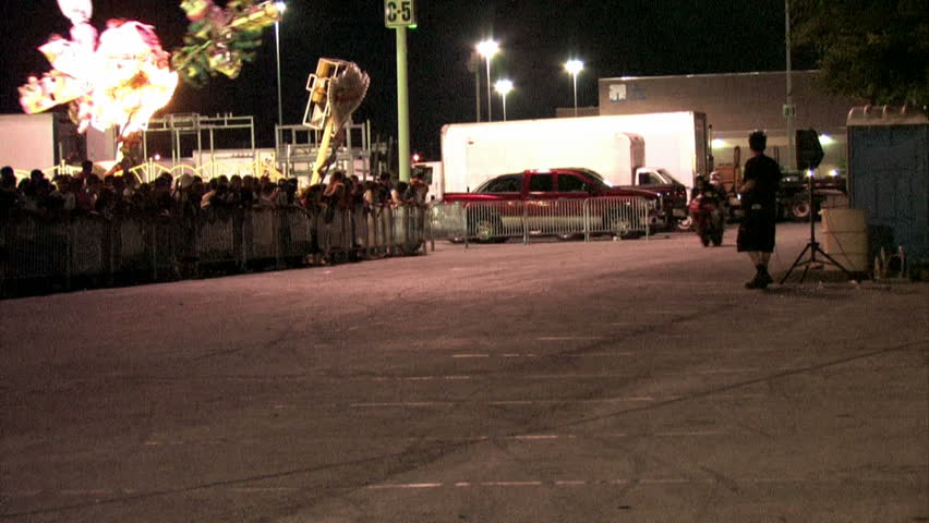 Stunt motorcycle rider doing a nose wheel ride at night. Carnival with bright lights and thrill rides.