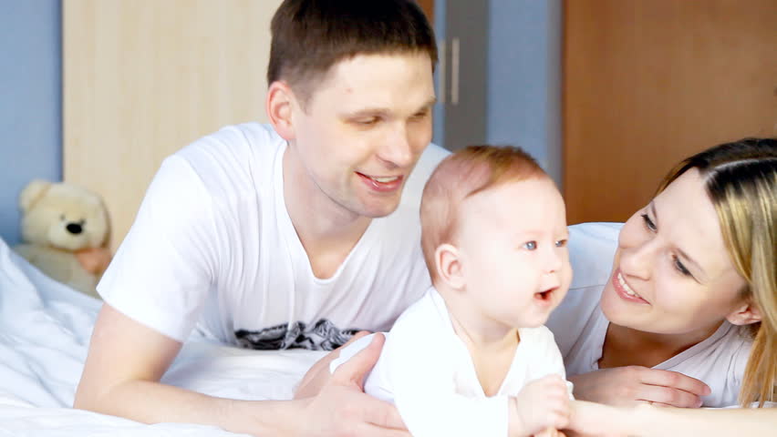 Happy family: father, mother and baby playing in the bedroom