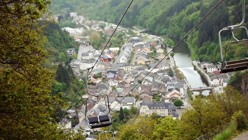 View of a valley in Luxembourg. The city of Vianden is in the distance. A chair lift is passing by.