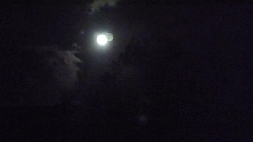 Simple Moon time lapse with dark night sky, forest evergreen trees, minimal clouds and moon flare.