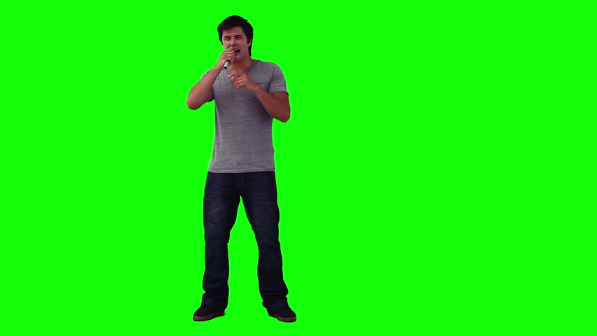 A man holding a microphone is singing in front of a green background