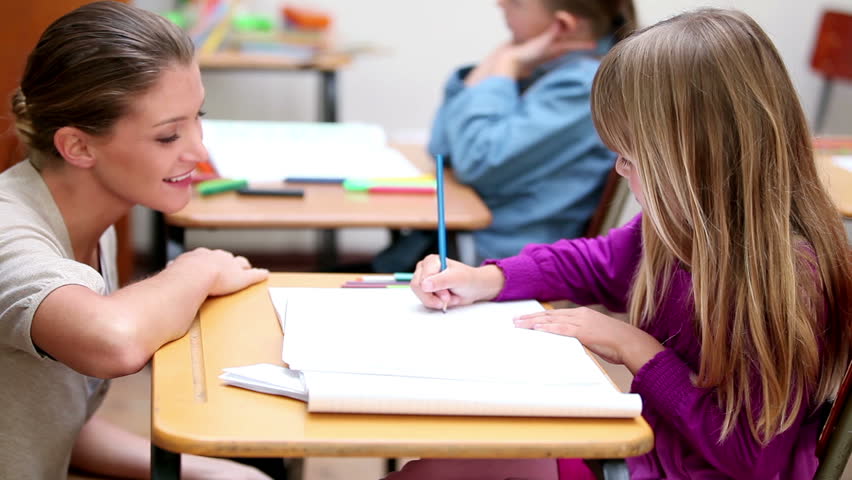 Happy teacher helping a pupil in the classroom