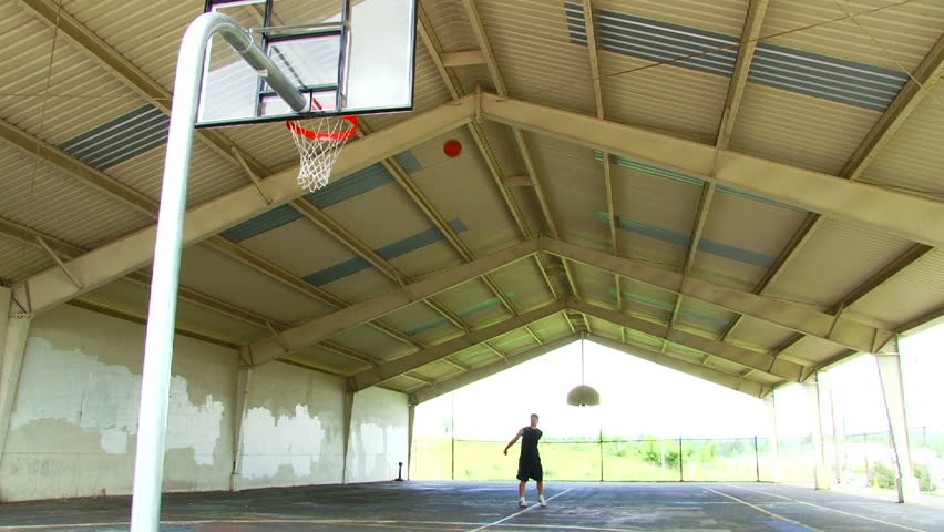 Man shoots basketball from half court, makes the shot and raises his arms in the air for victory. Slow Motion available.