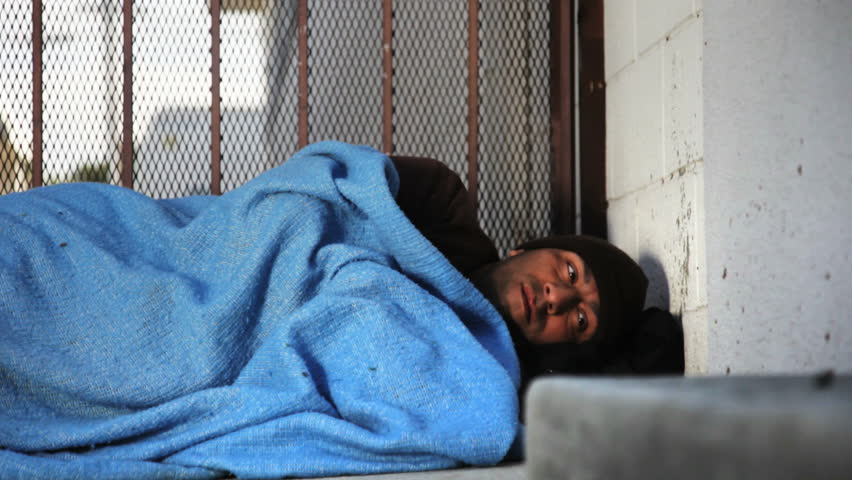 Homeless man trying to sleep on the sidewalk