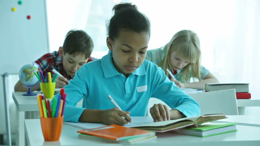 Pensive pupils doing tasks during the lesson, African-American girl in the foreground