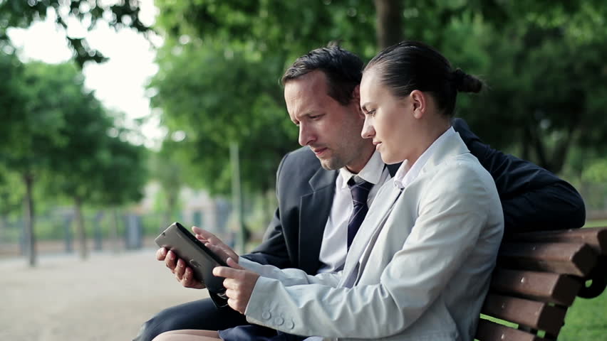 Business couple with tablet computer in the park, dolly shot
