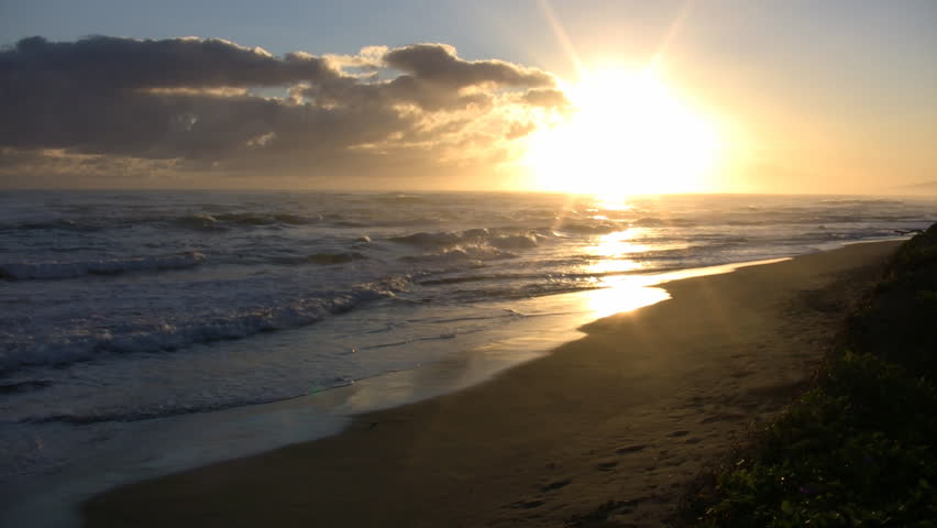 Waves gently wash up onto the beach, then recede as the sun starts to rise. (High Definition)