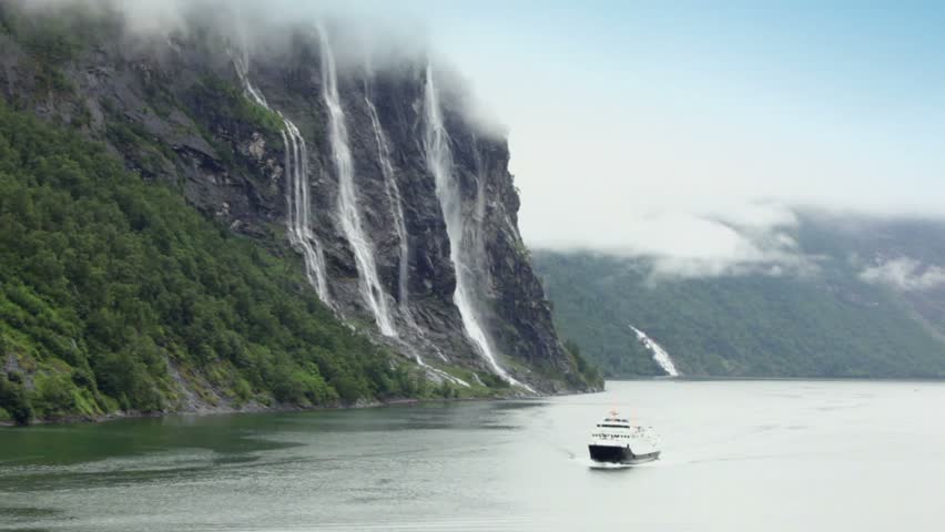 Ship floats by fiord near Seven Sisters waterfall on rocky mountain at shore in Norway
