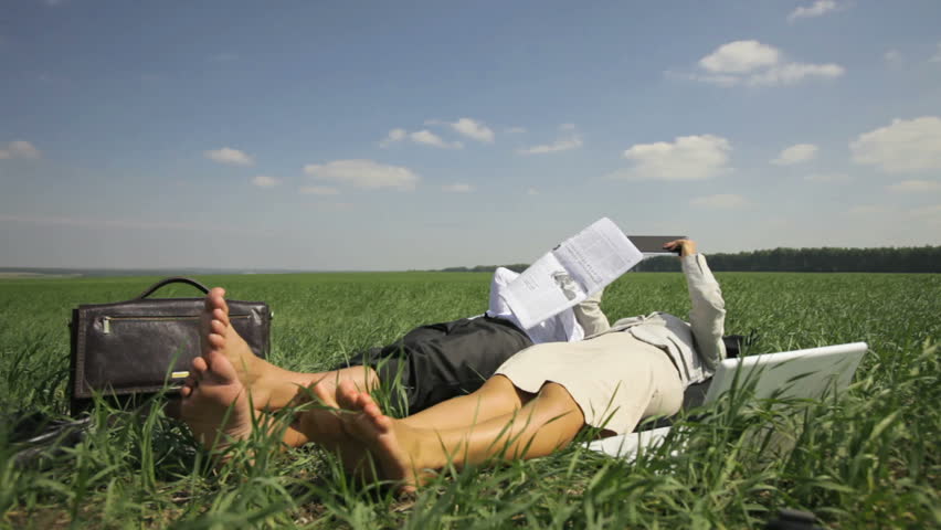 Relaxed office people lying on the grass and conducting business affairs