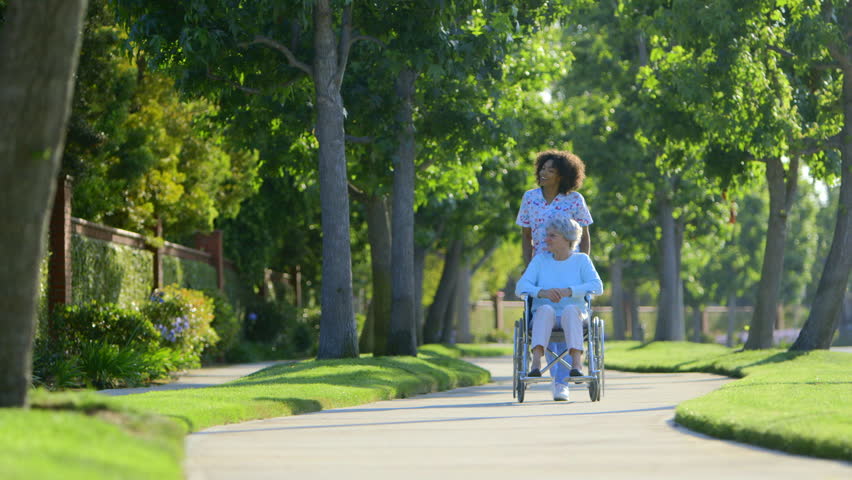 Nurse walking with elderly woman in wheelchair