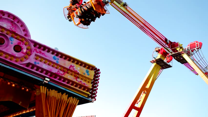 Large swinging ride in motion against a blue sky in an amusement park during the day time.