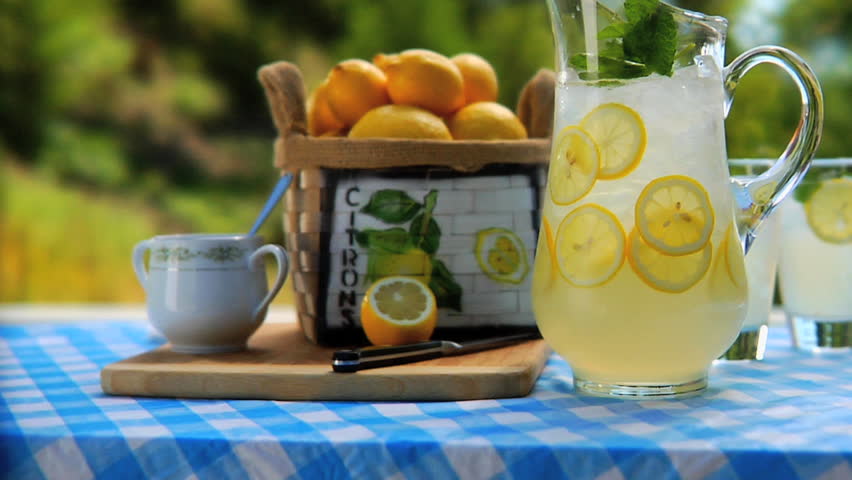 Man removing 2 glasses of lemonade from table with Pitcher of lemonade outside