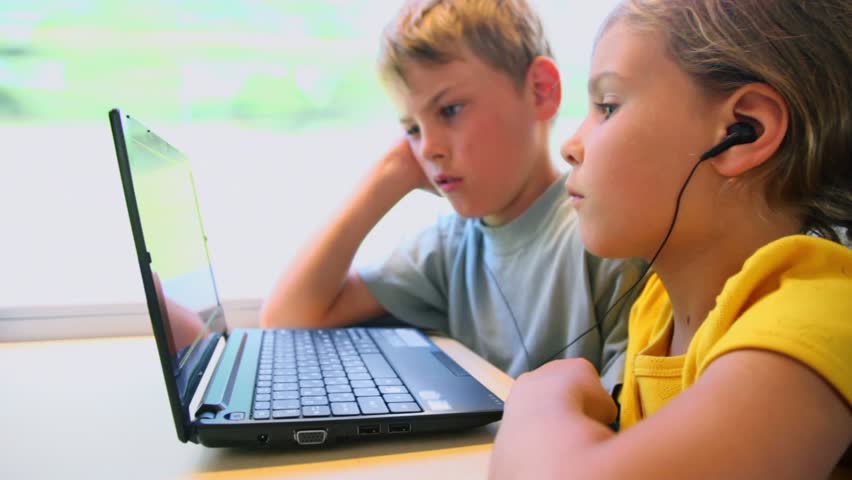 Two kids boy and little girl watch on netbook when sits at train near window