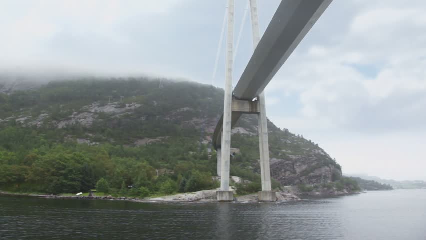 Huge pendant bridge at coast with forest on mountains under cloudy sky