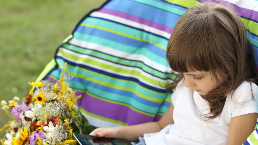 Schoolgirl with a tablet pc sitting in a chair outdoors
