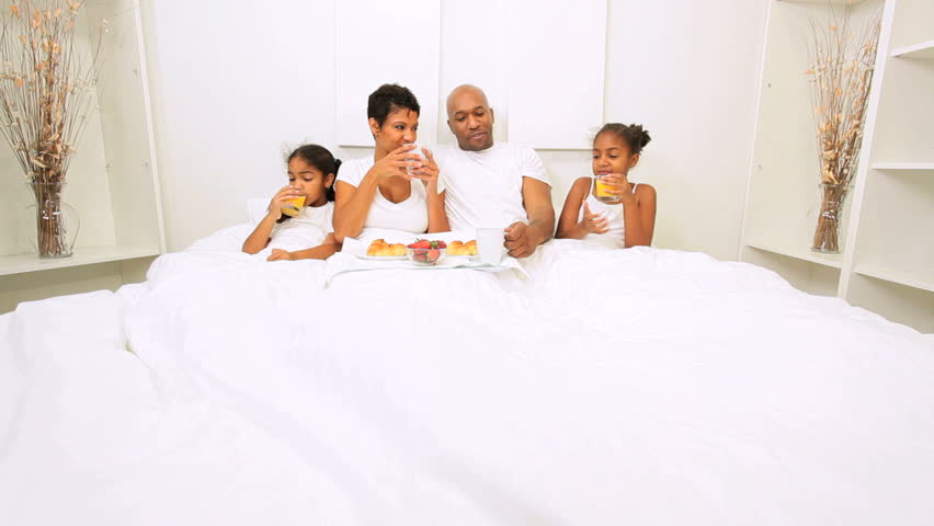 African American family relaxing sharing breakfast bed weekend