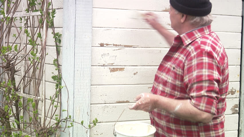 Elderly man painting his summer cottage