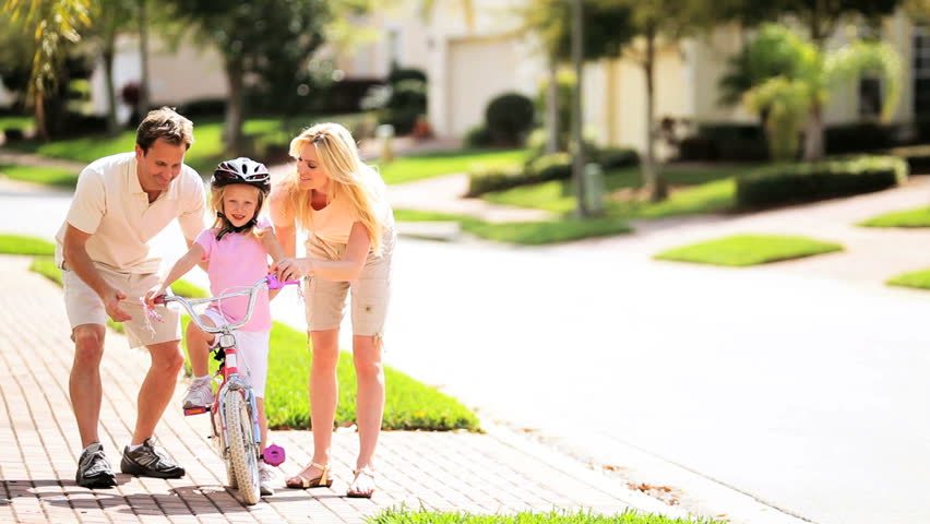 Young blonde girl being taught to ride a bicycle by her parents