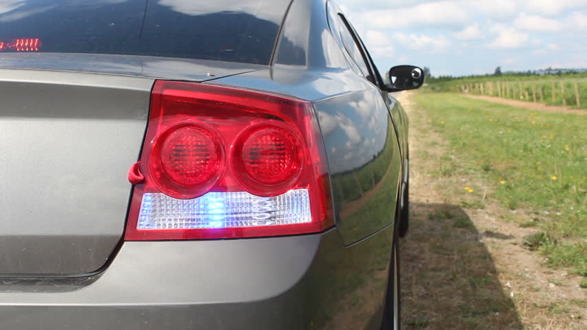 An unmarked police cruiser waits patiently on the side of a road/Flashing Lights on an Unmarked Police Cruiser/Lights flash on an unmarked police cruiser on the side of a road. 